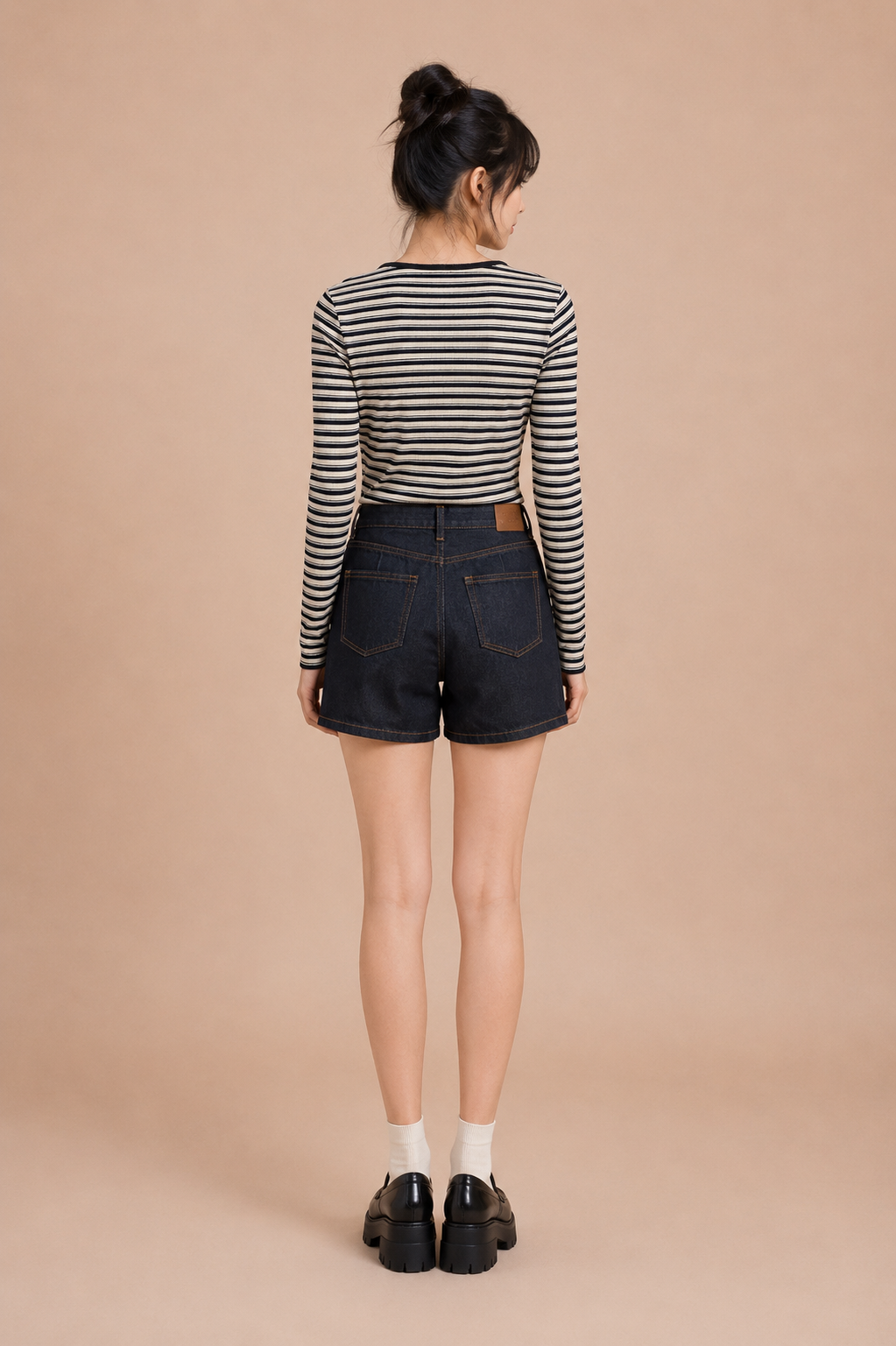 Woman wearing a striped long-sleeve shirt and black shorts against a beige background