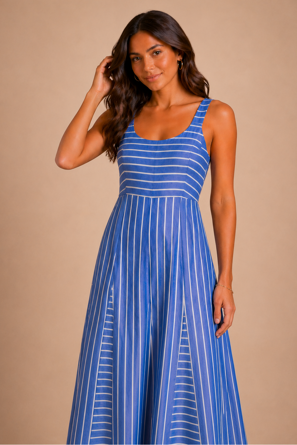 A woman in front of a beige backdrop wearing a striped blue maxi dress.