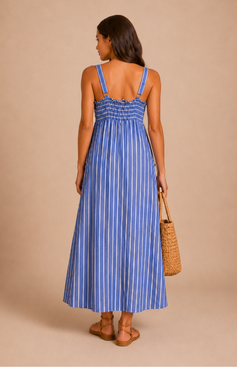 A woman in front of a beige backdrop wearing a striped blue maxi dress.