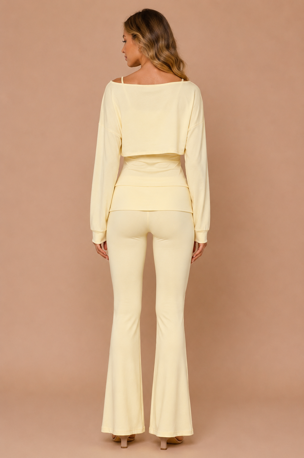 Woman wearing a light yellow long-sleeve top and flared pants against a beige background