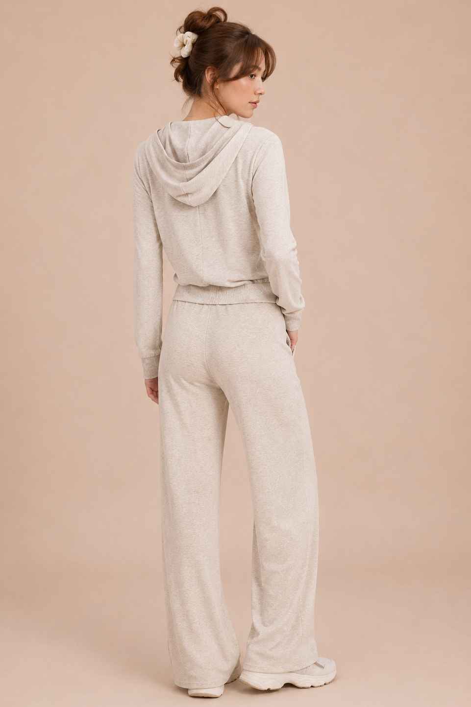 Woman wearing a light gray hoodie and pants on a beige background