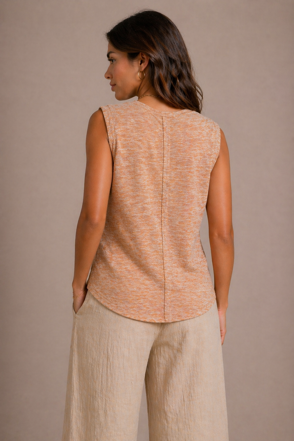 Woman wearing a beige sleeveless top and pants against a brown background