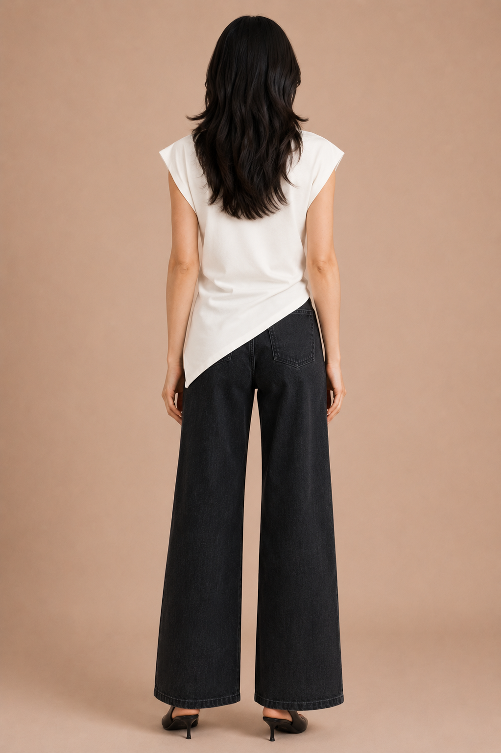 Woman wearing white asymmetrical top and black jeans against beige backdrop.