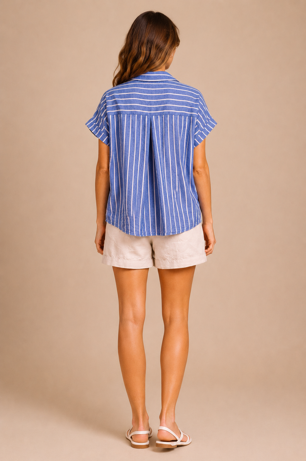 Woman wearing a blue striped shirt and white shorts against a beige background